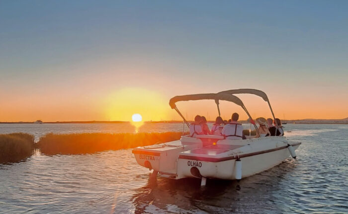 Guests engaging in a guided sunset boat tour from Faro, admiring the changing colors of the sky over Ria Formosa.