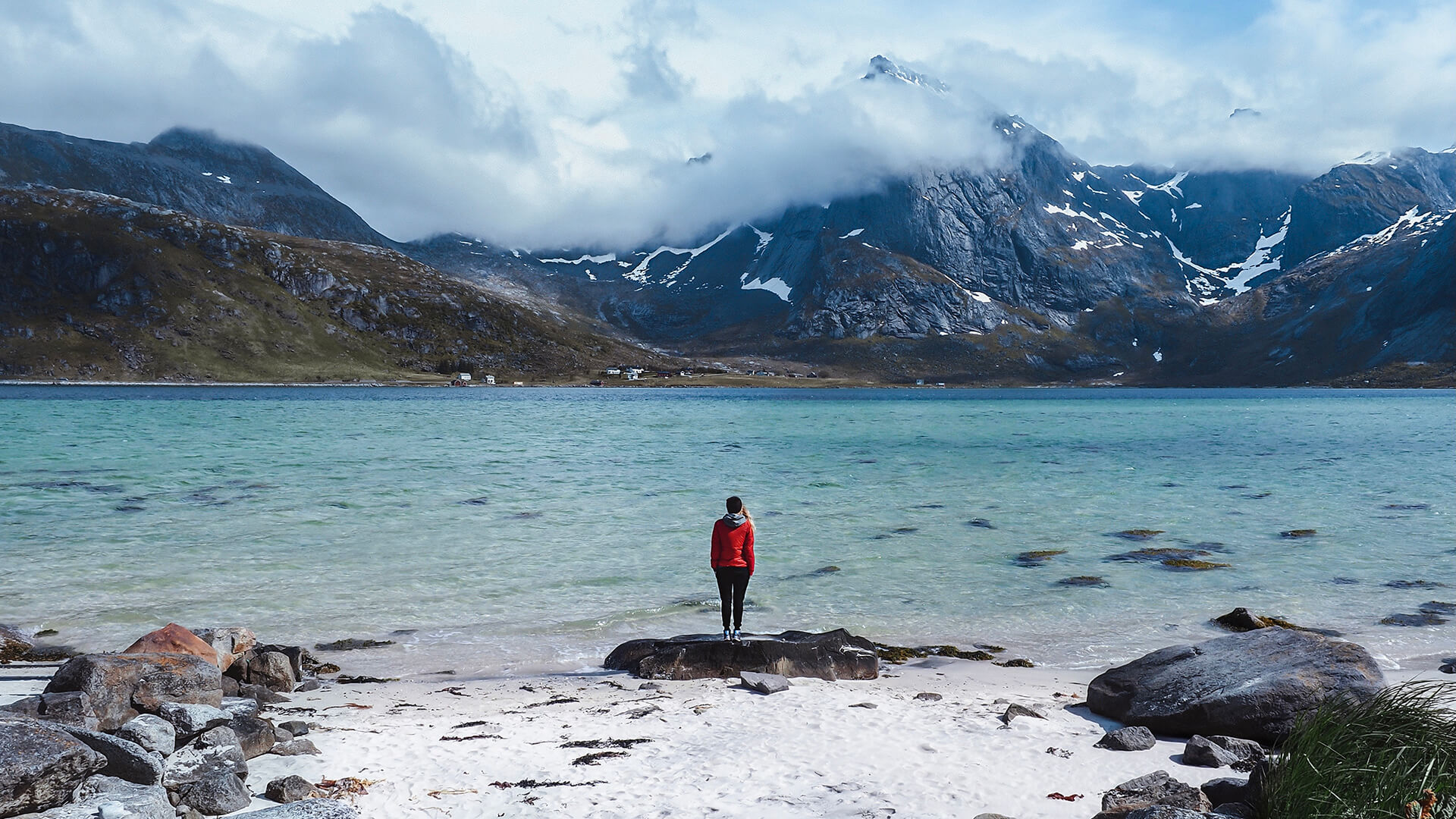 Imagem de um viajante parado junto às águas costeiras enevoadas nas Ilhas Lofoten, Noruega – ao fundo, altas montanhas avultam